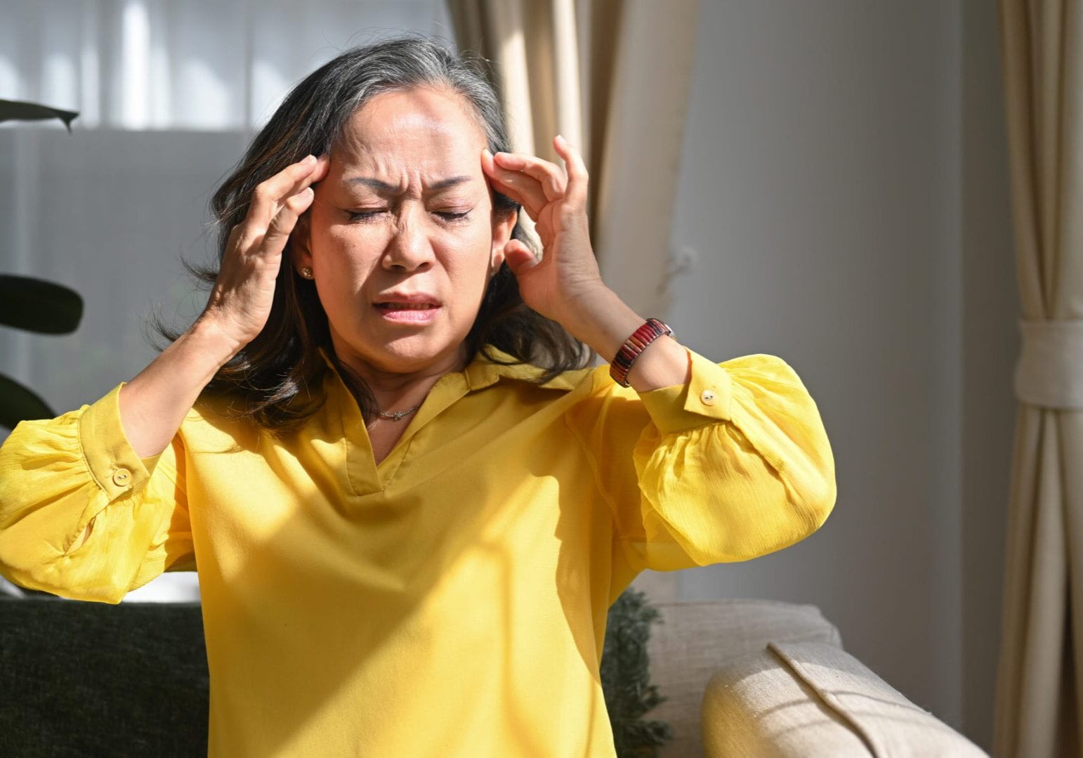 Upset mature woman touching her head suffering from head ache, migraine or dizziness. Age, medicine, health care and people concept.